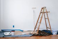 Ladder, roller, and paint set out on drop cloths in a room prepped for painting
